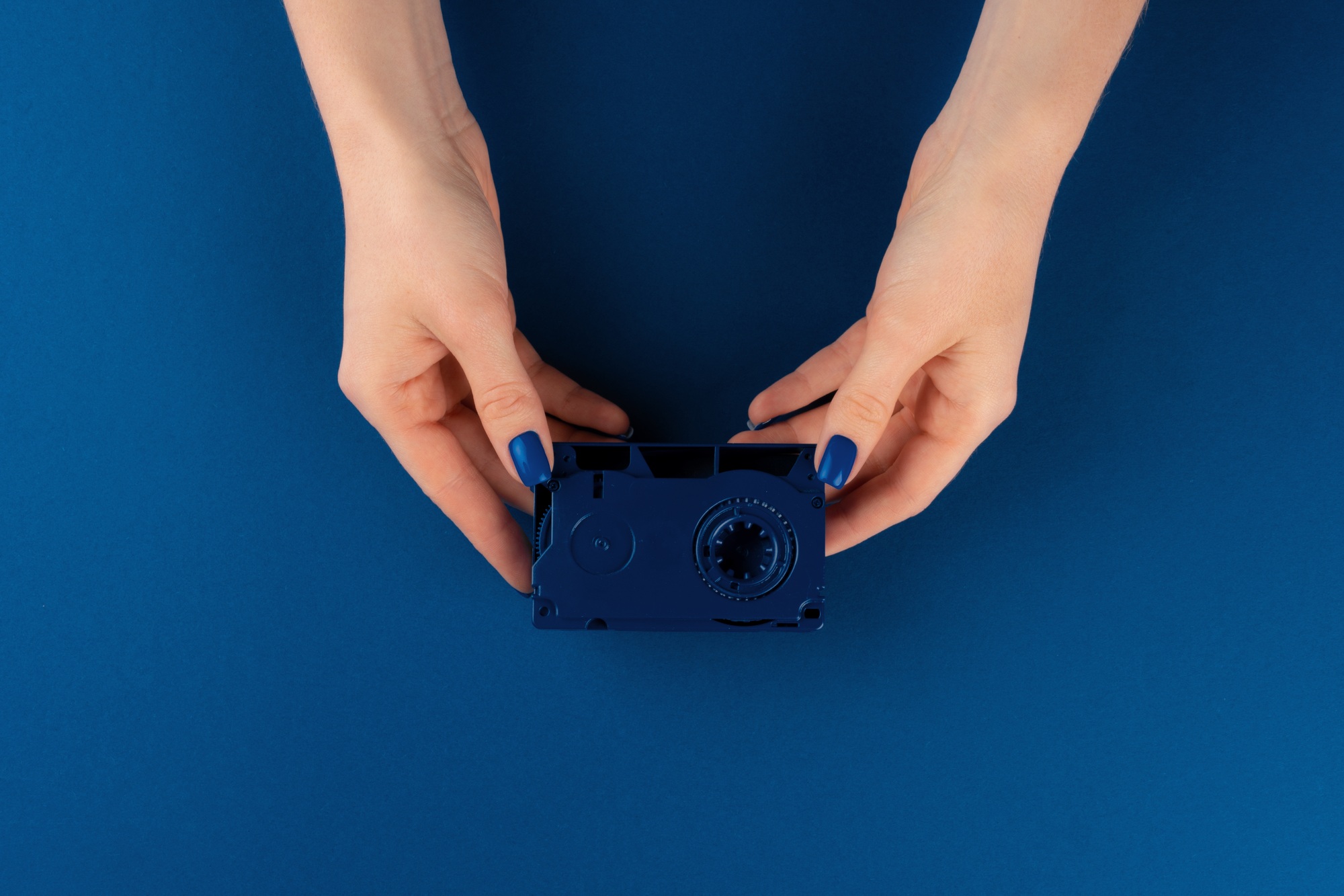 Mini video cassette in female hands against classic blue background